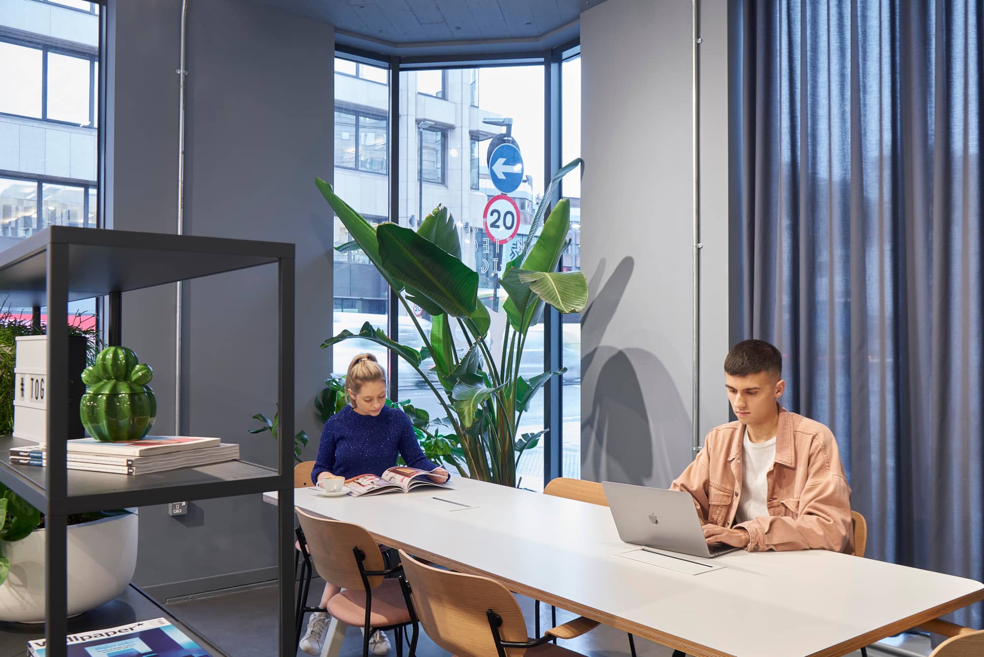 Man working on his laptop and woman reading at a table at 133 Whitechapel High Street.