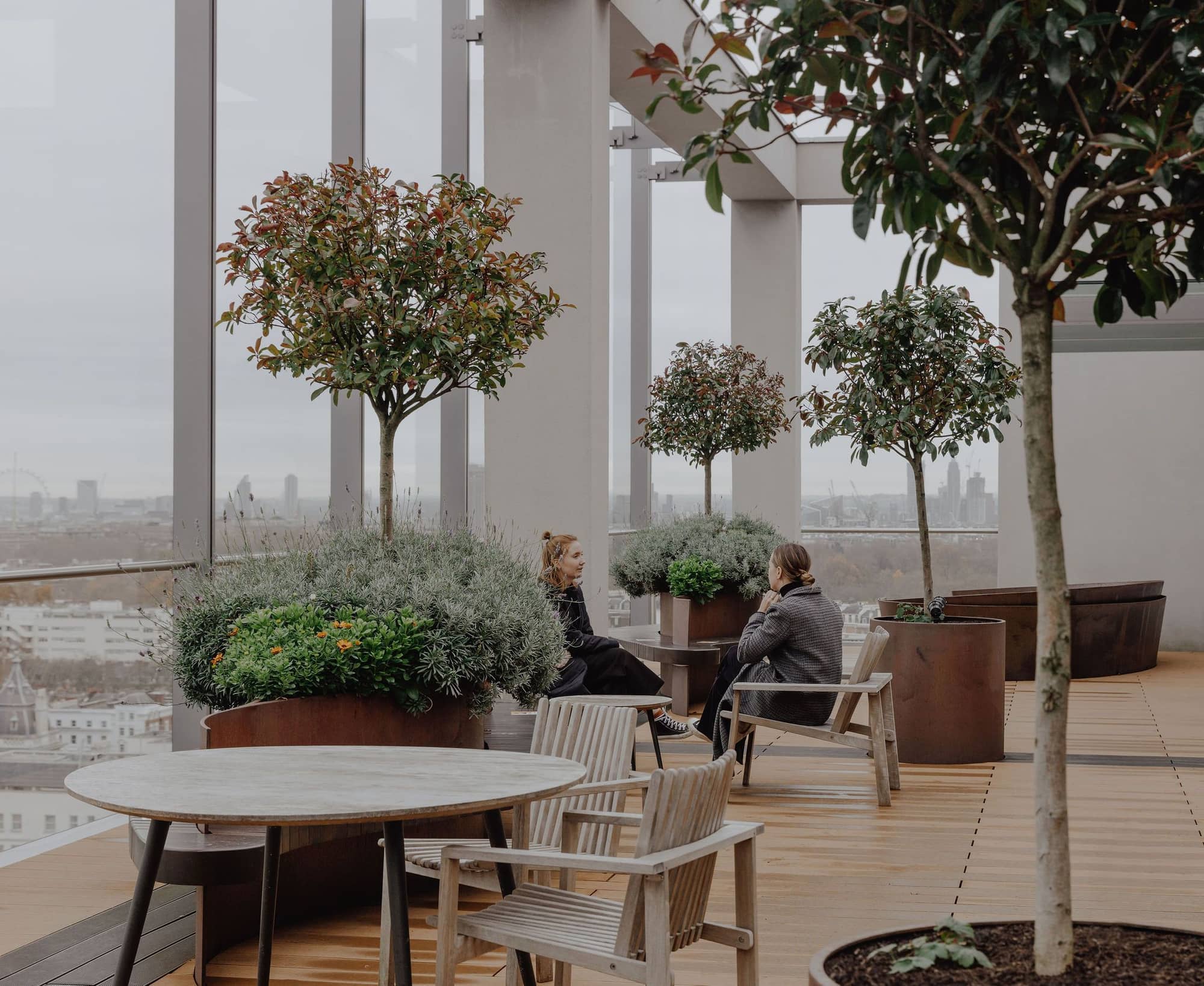 Two women talking on the roof terrace surrounded by plants and a panoramic view of London.