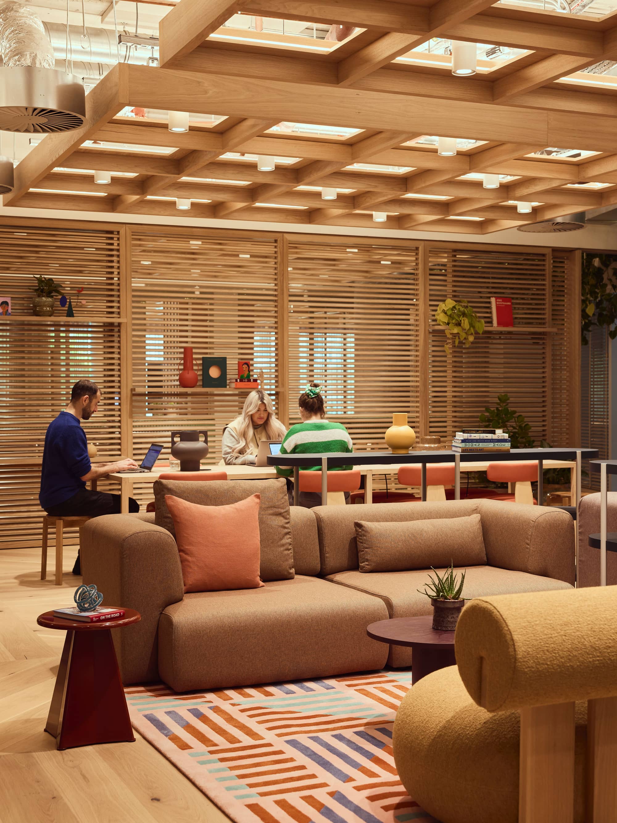 Cosy communal space with desks, chairs, a sofa and plants.