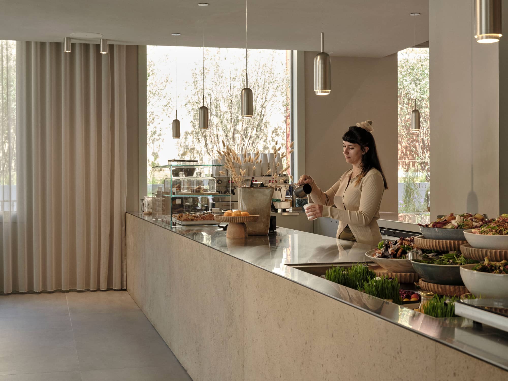 Woman pours coffee from behind a cream, marble bar at the café in Chancery House.